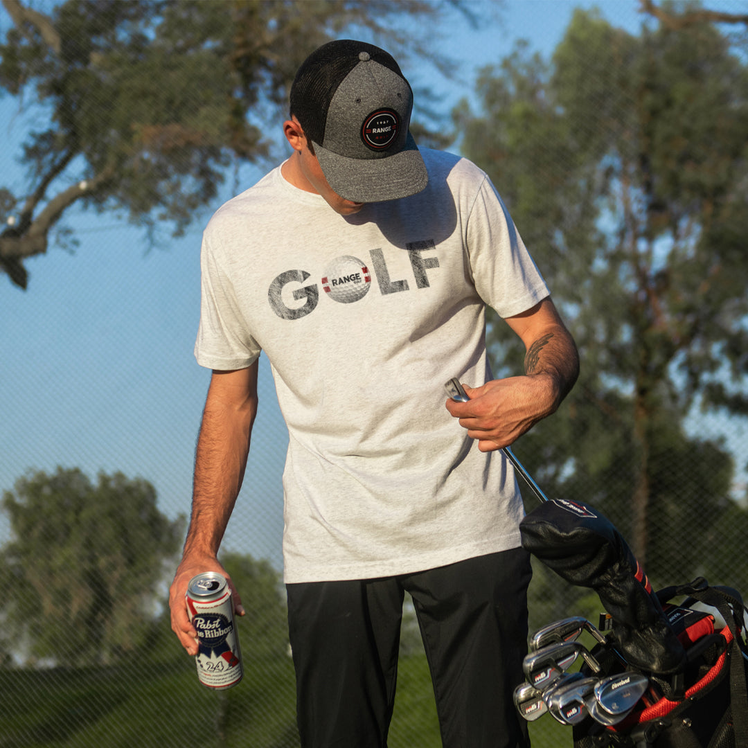 man grabbing golf clubs while wearing white t-shirt with range golf ball as "o" in "golf" design